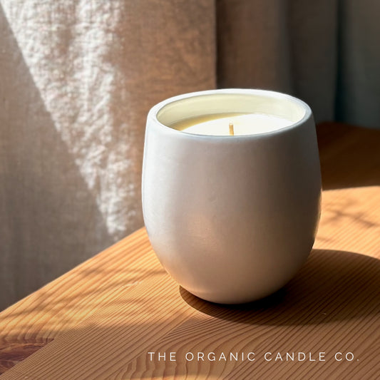 White organic candle in a ceramic vessel on a wooden surface with 'The Organic Candle Co.' branding.