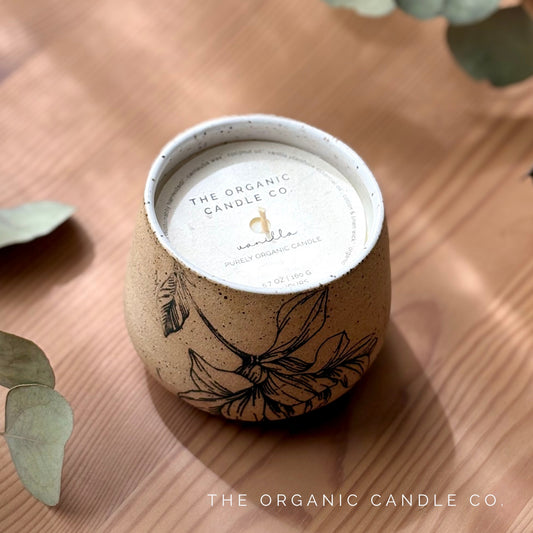 Organic candle in ceramic vessel with botanical design, labeled with 'The Organic Candle Co' label on a wooden surface