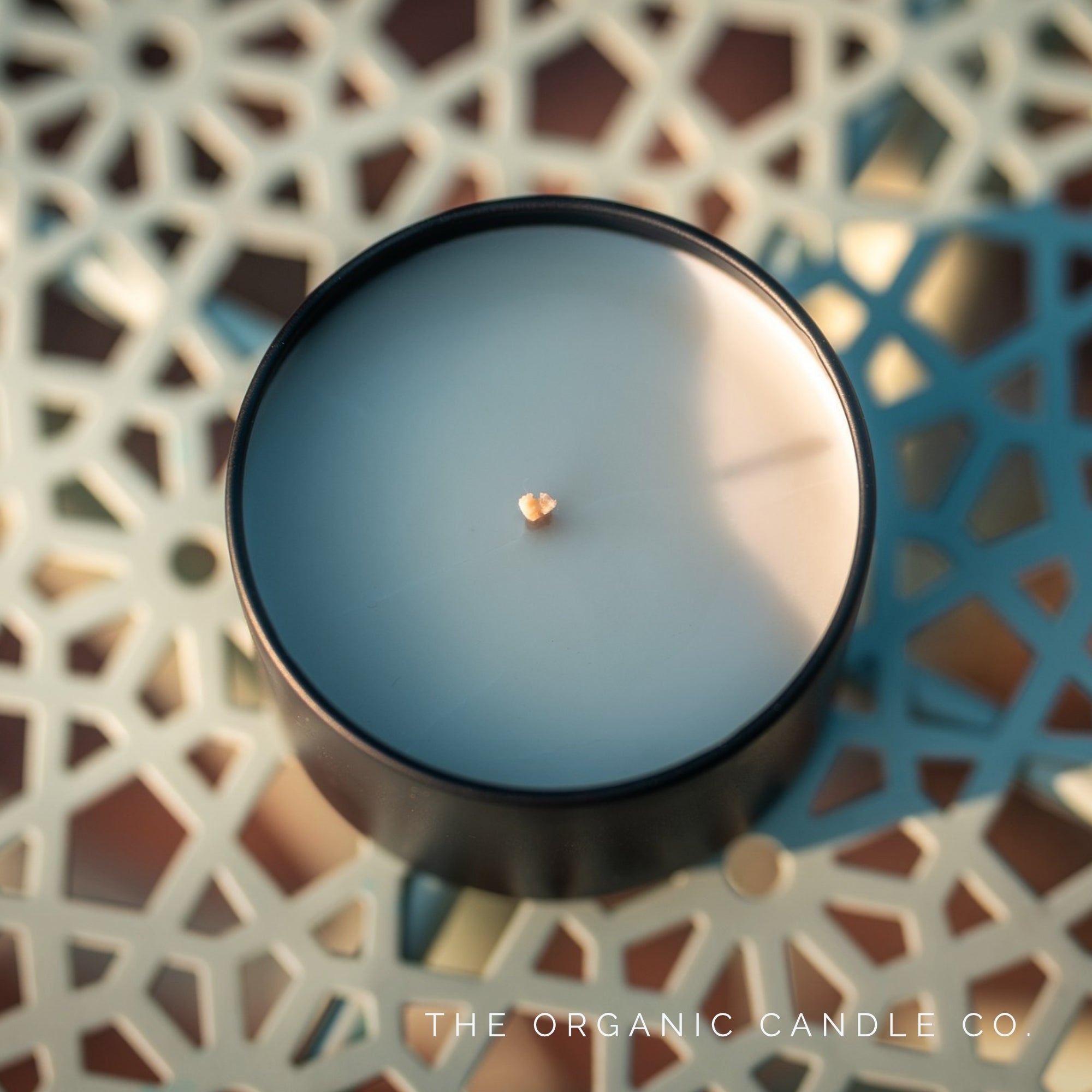 Black candle on a decorative surface, branded 'The Organic Candle Co'.