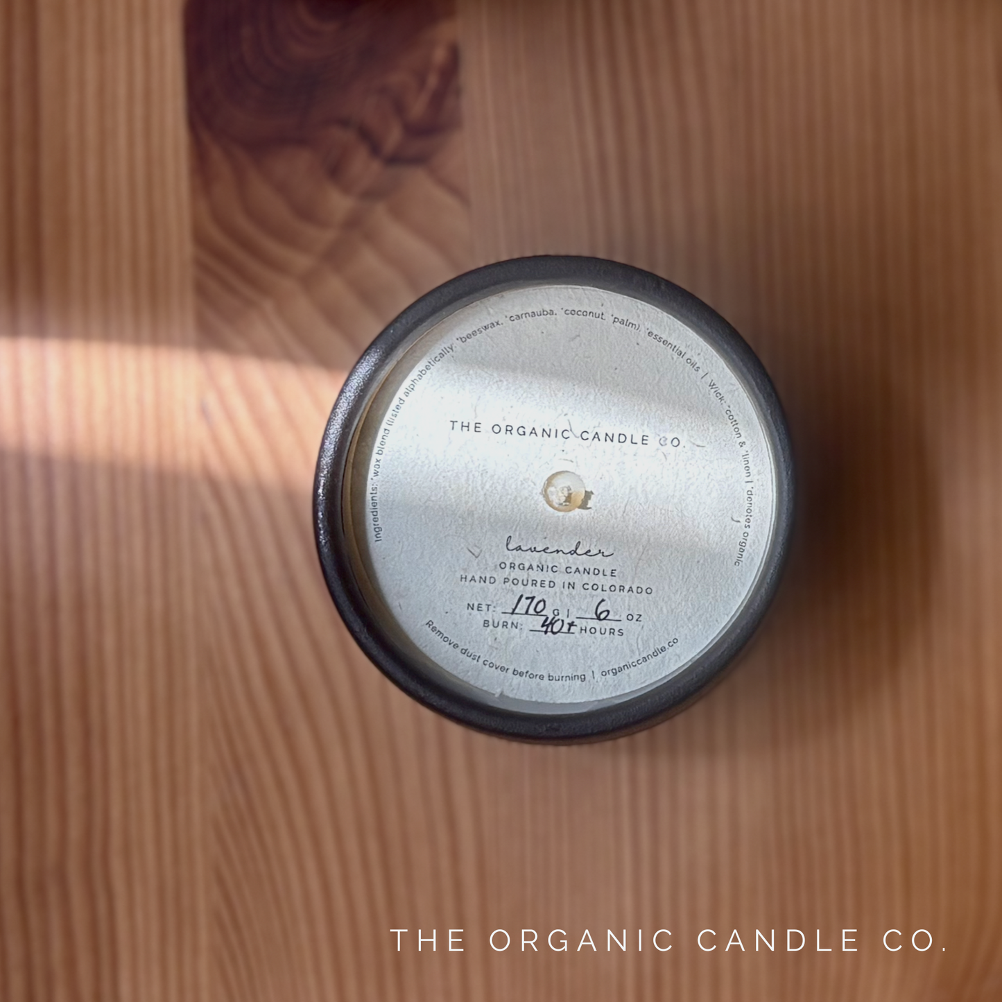Black candle with label on a wooden surface, featuring 'The Organic Candle Co.'