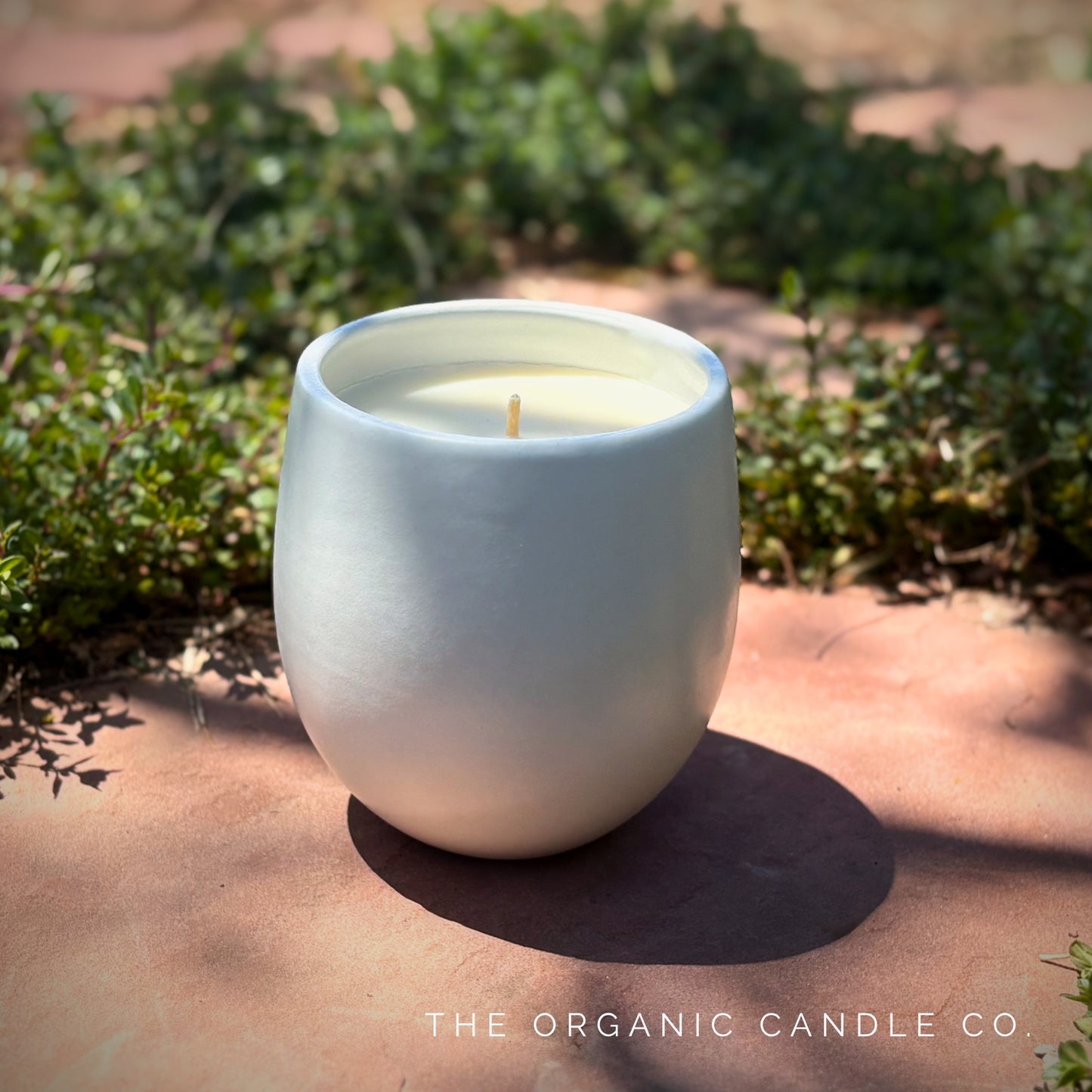White organic candle in a ceramic vessel on a stone surface with greenery in the background, featuring 'The Organic Candle Co.'