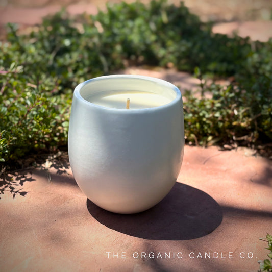 White organic candle in a ceramic vessel on a stone surface with greenery in the background, featuring 'The Organic Candle Co.'