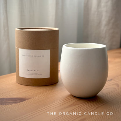 White organic candle in ceramic vessel and brown cardboard tube with label on a wooden surface, featuring 'The Organic Candle Co.'