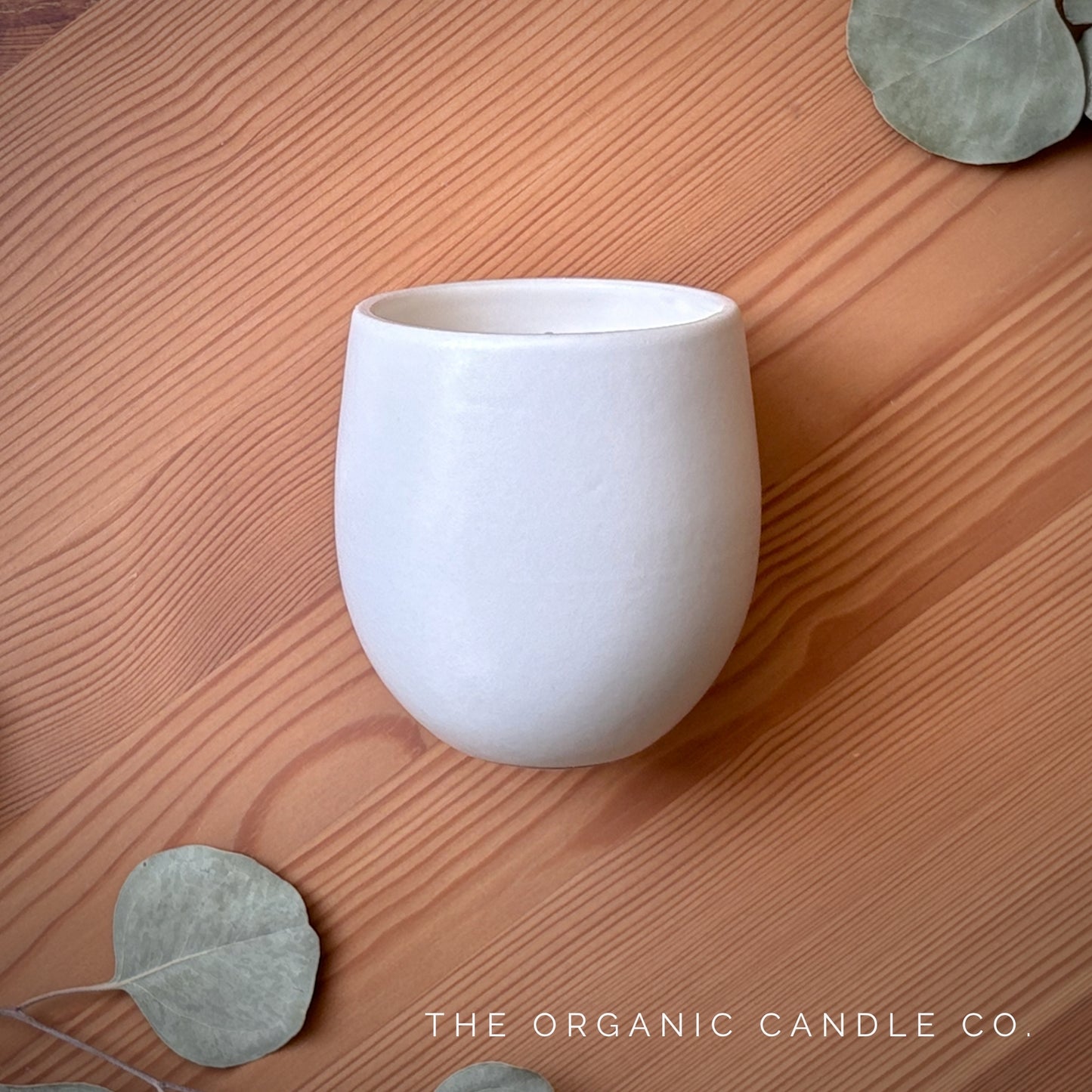 White organic candle in a ceramic vessel on a wooden surface with 'The Organic Candle Co' branding.