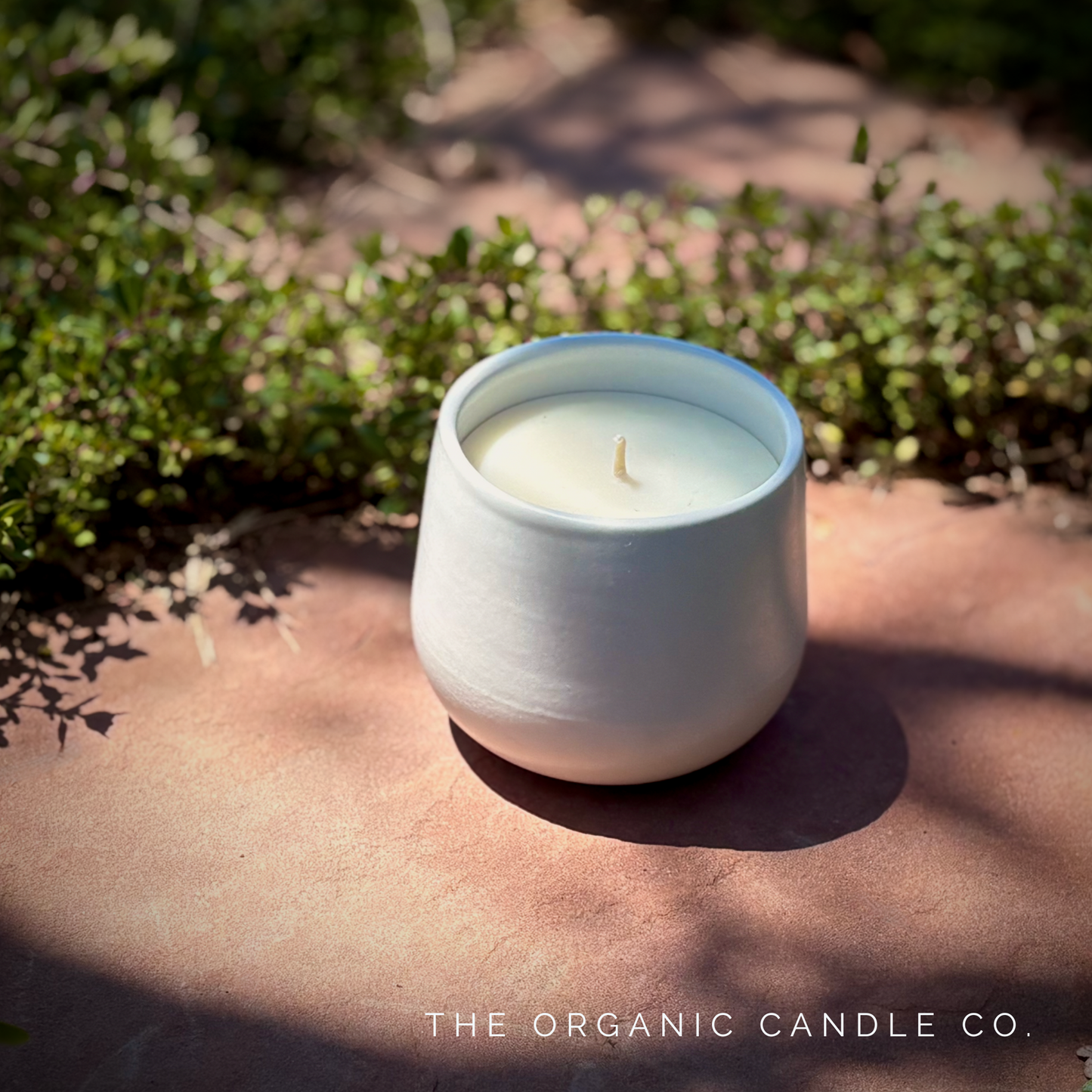 White organic ceramic candle on a stone surface with greenery in the background, branded 'The Organic Candle Co'.