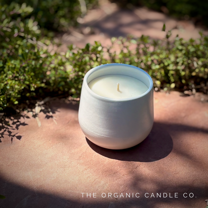 White organic ceramic candle on a stone surface with greenery in the background, branded 'The Organic Candle Co'.