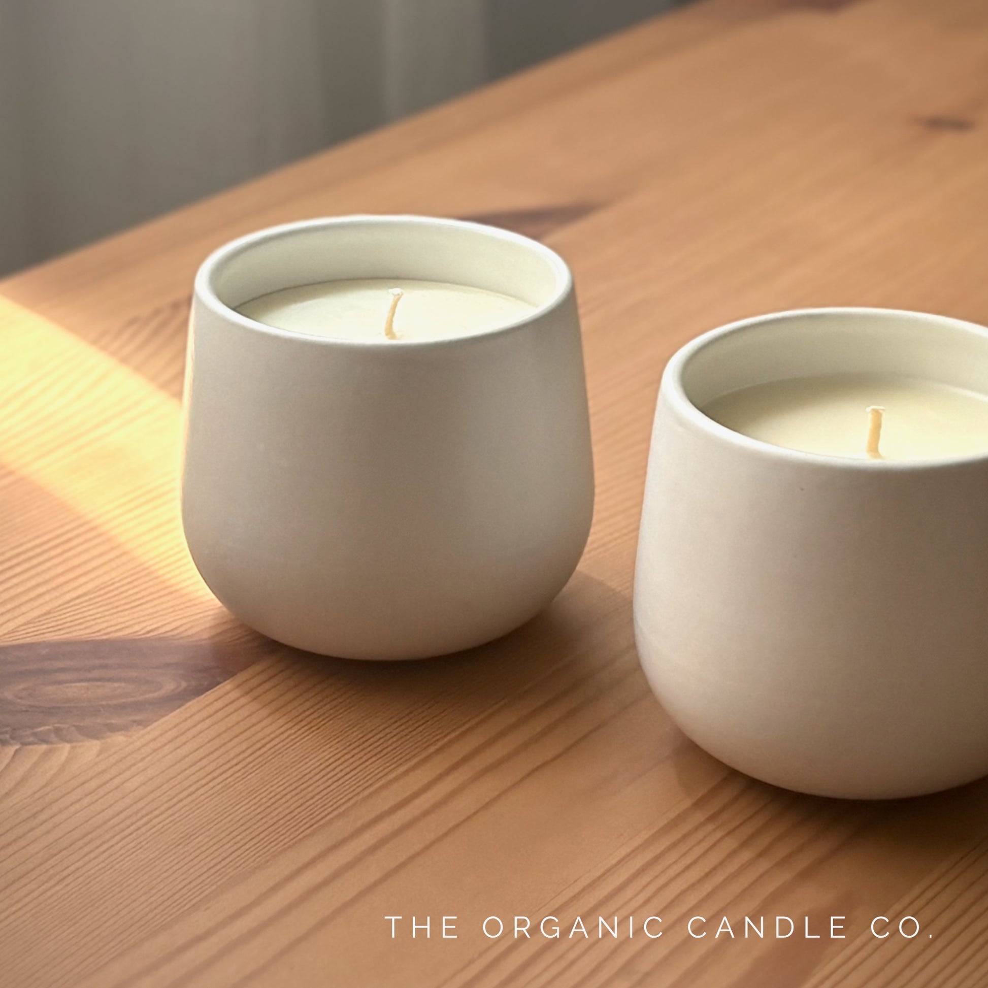 Two white organic candles on a wooden surface with 'The Organic Candle Co.' brand