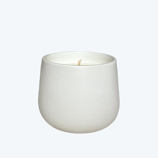 White organic candle in a ceramic vessel on a neutral background