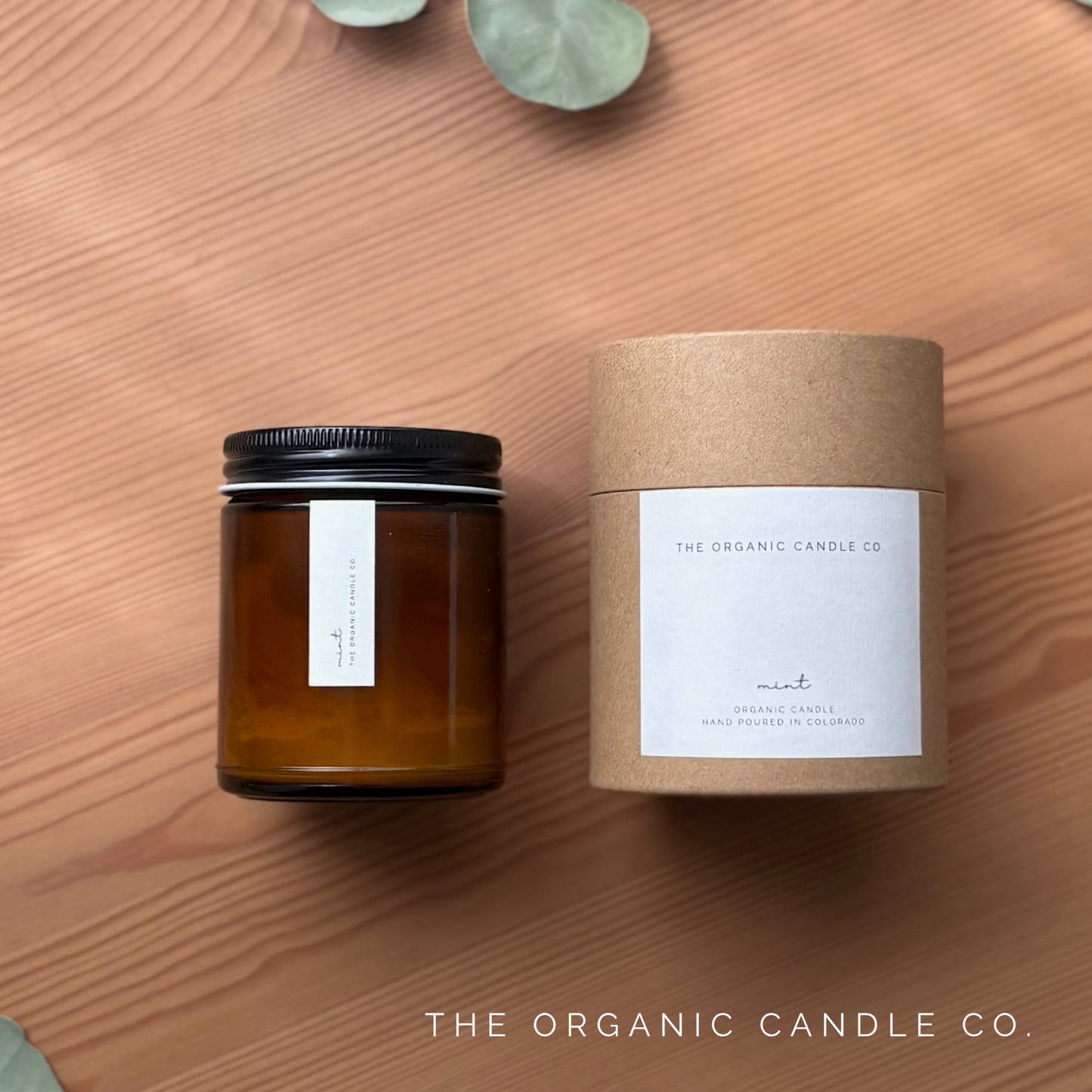 Brown candle and packaging with 'The Organic Candle Co.' branding on a wooden surface.