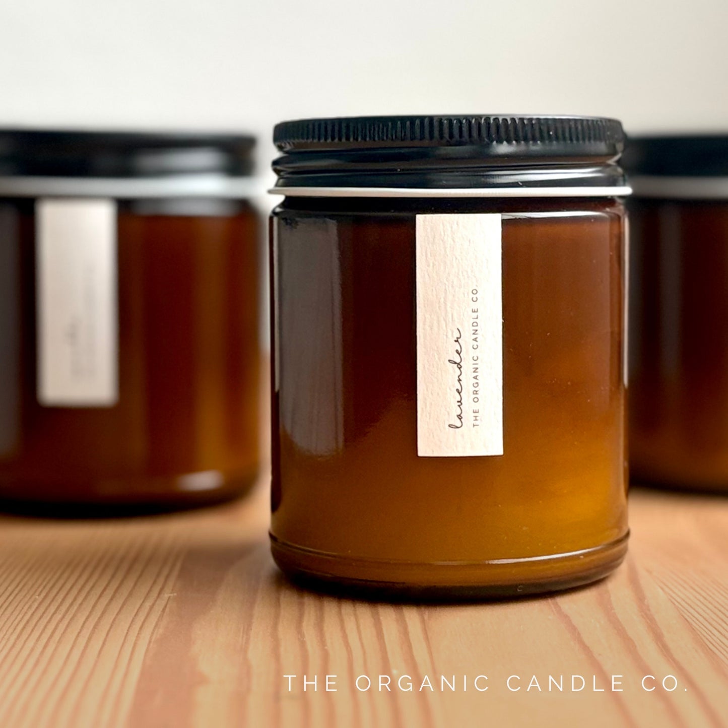 Organic candle in an amber glass vessel with black lid and label on a wooden surface, featuring 'The Organic Candle Co.'