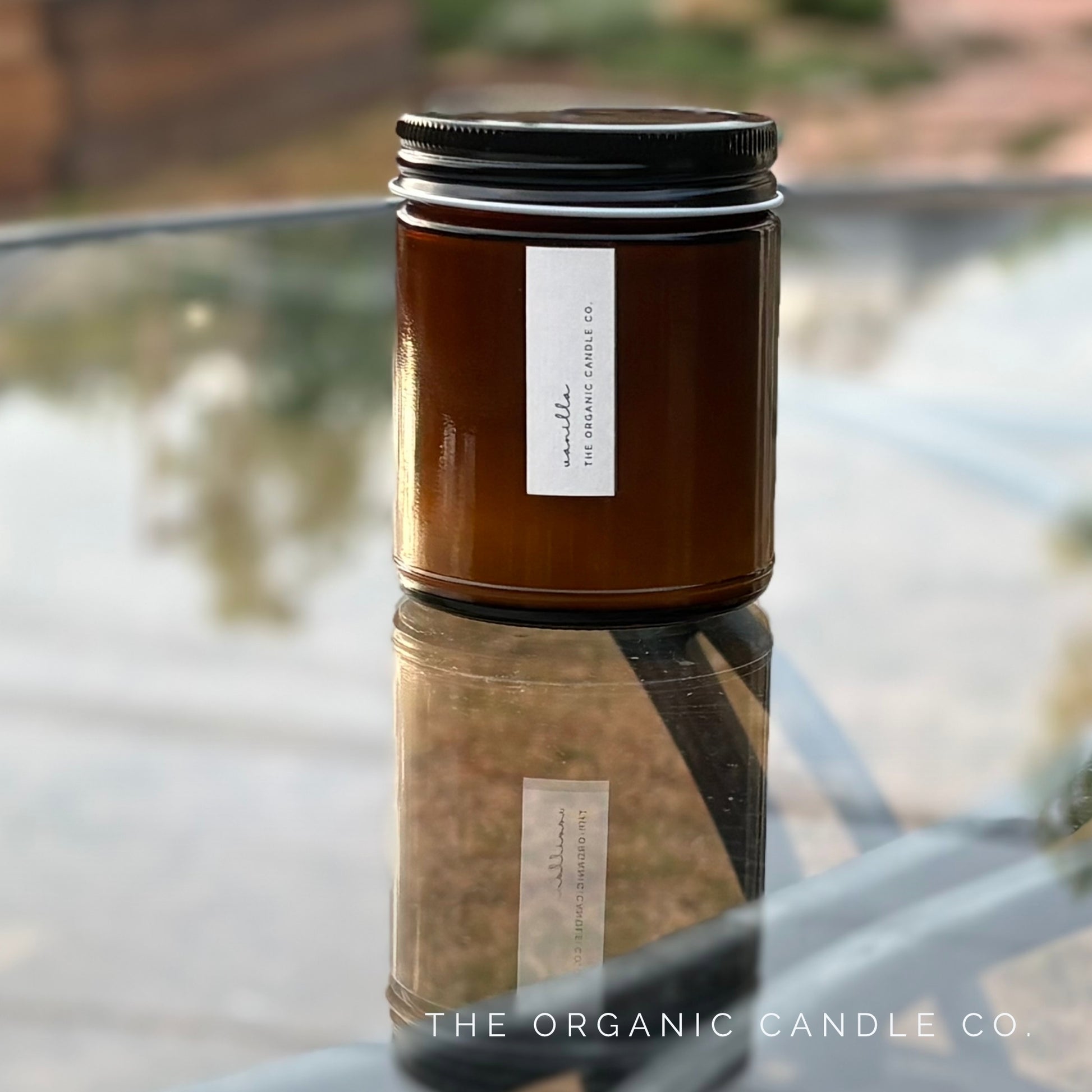 Organic candle in an amber jar with black lid on a reflective surface outdoors