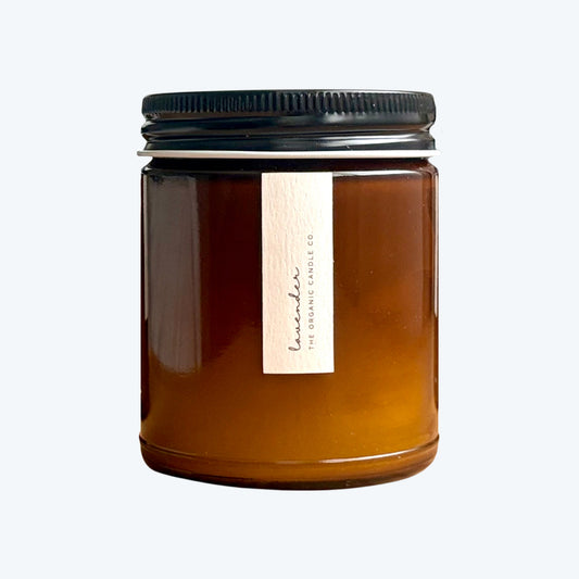 Organic candle in an amber glass vessel with a black lid on a neutral background