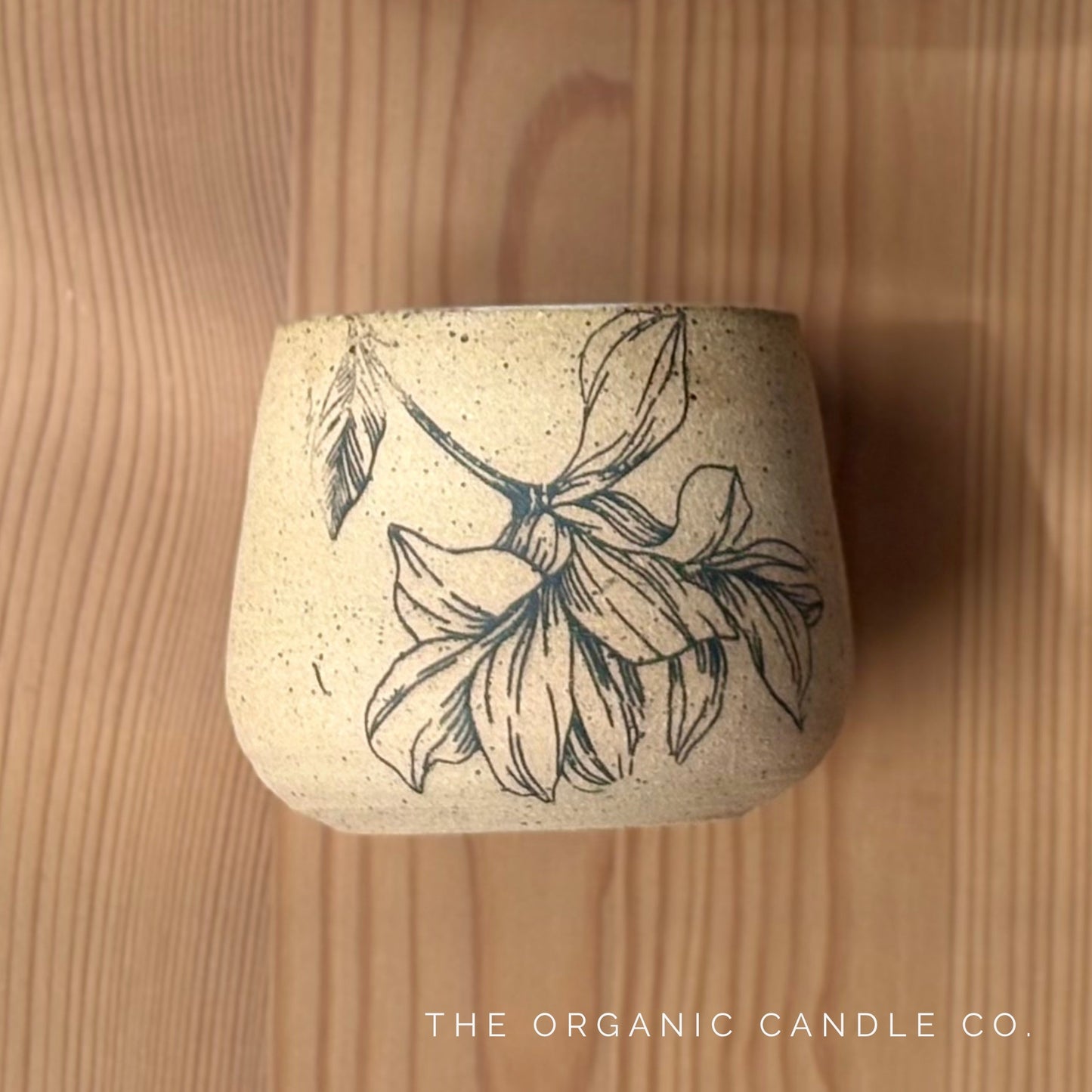 Organic candle in ceramic vessel with botanical design on a wooden surface, branded 'The Organic Candle Co'.