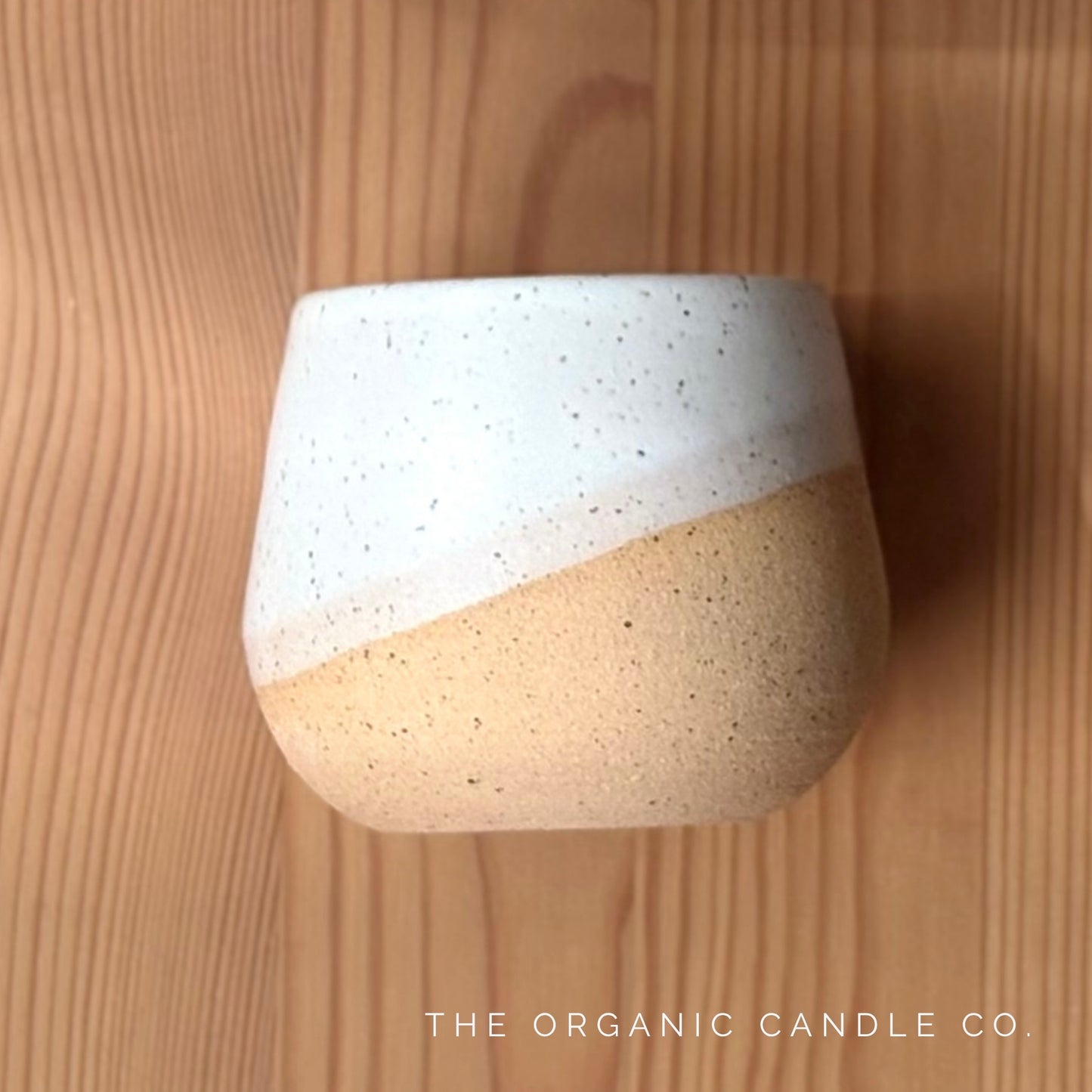 Organic candle in a two-toned ceramic vessel on a wooden surface with 'The Organic Candle Co.' branding.