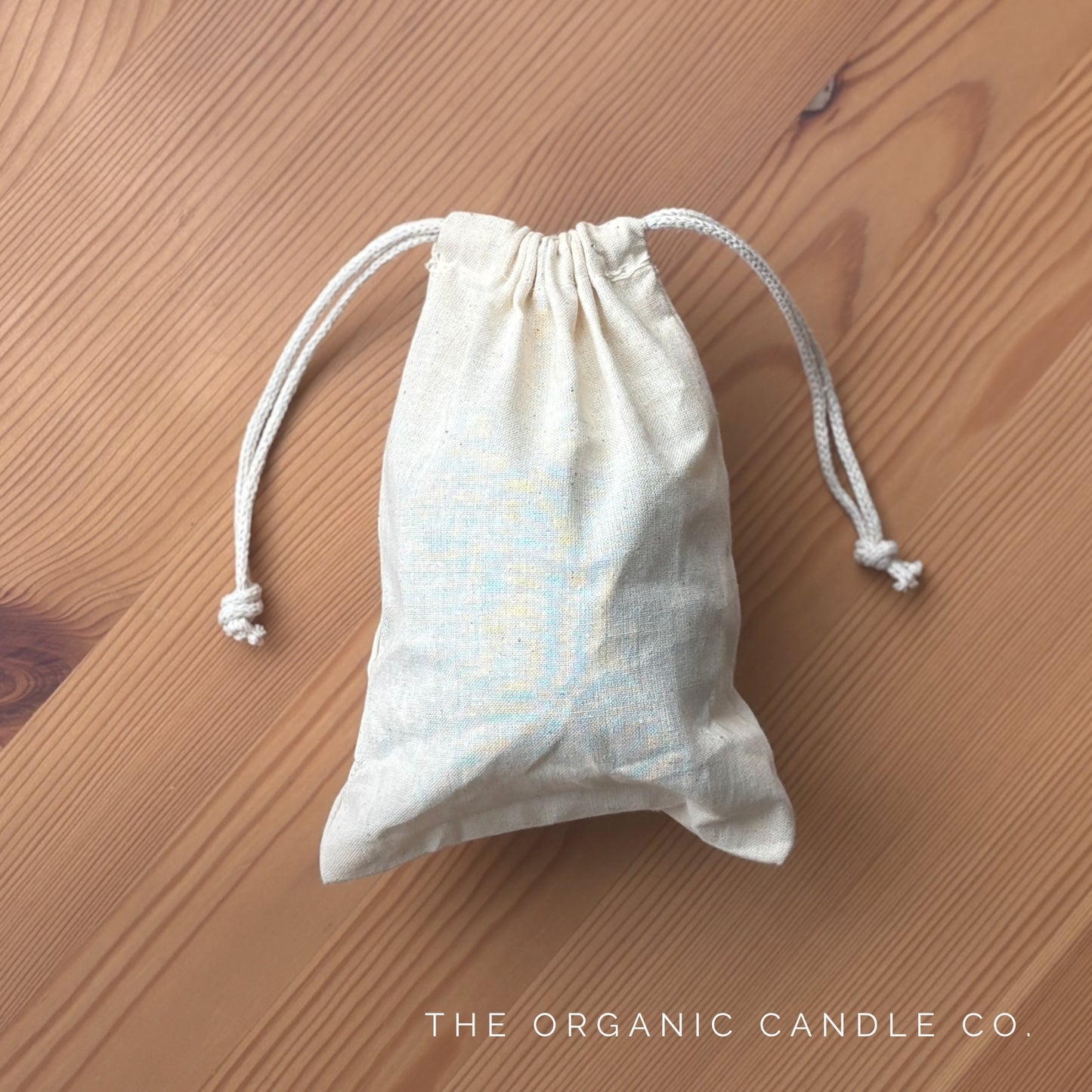 Small drawstring bag on a wooden surface with 'The Organic Candle Co.' branding.