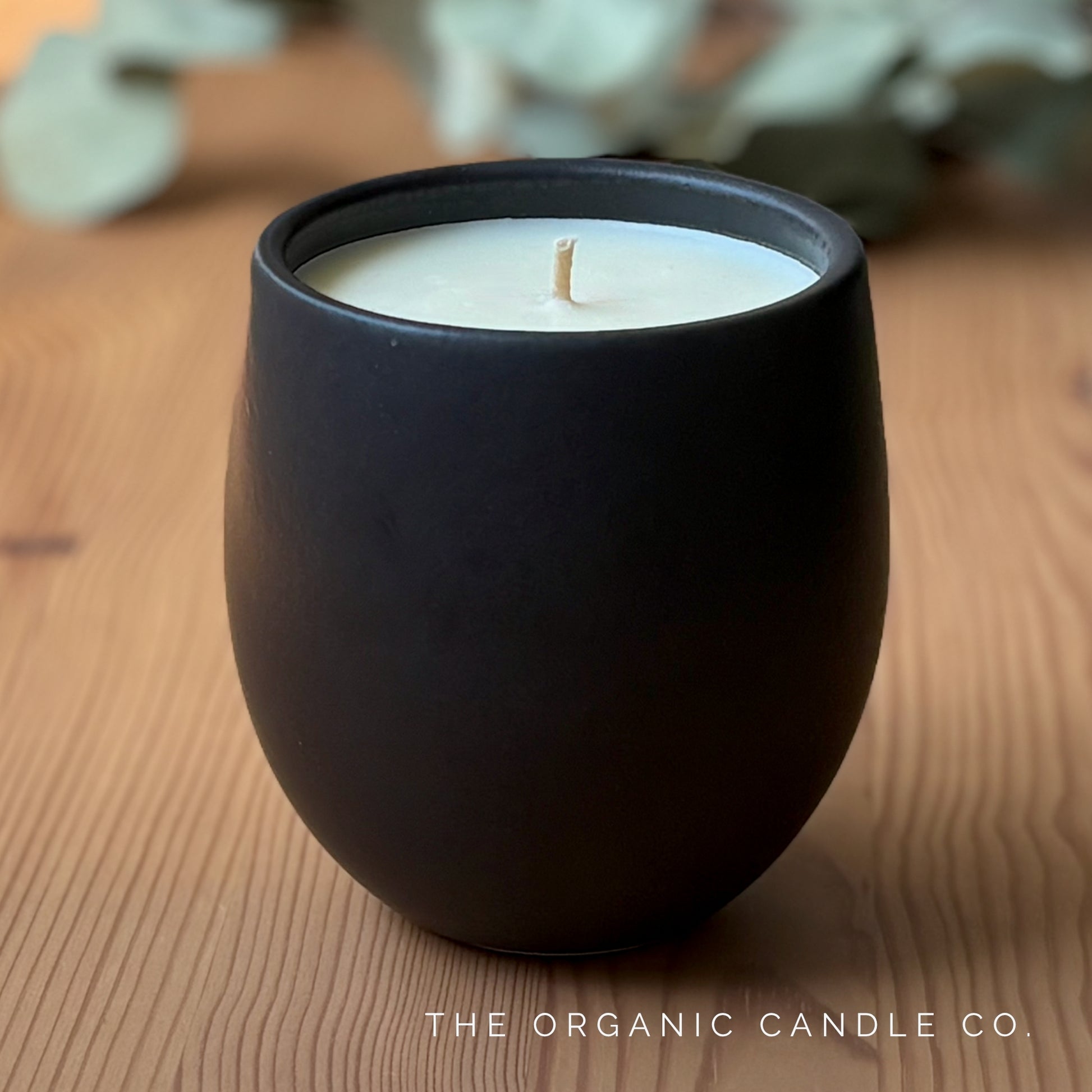 Organic candle in black ceramic vessel on a wooden surface, featuring 'The Organic Candle Co.'