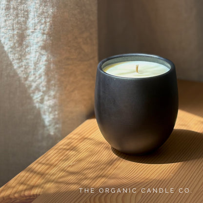 Organic candle in black ceramic vessel on a wooden surface with 'The Organic Candle Co.' branding.