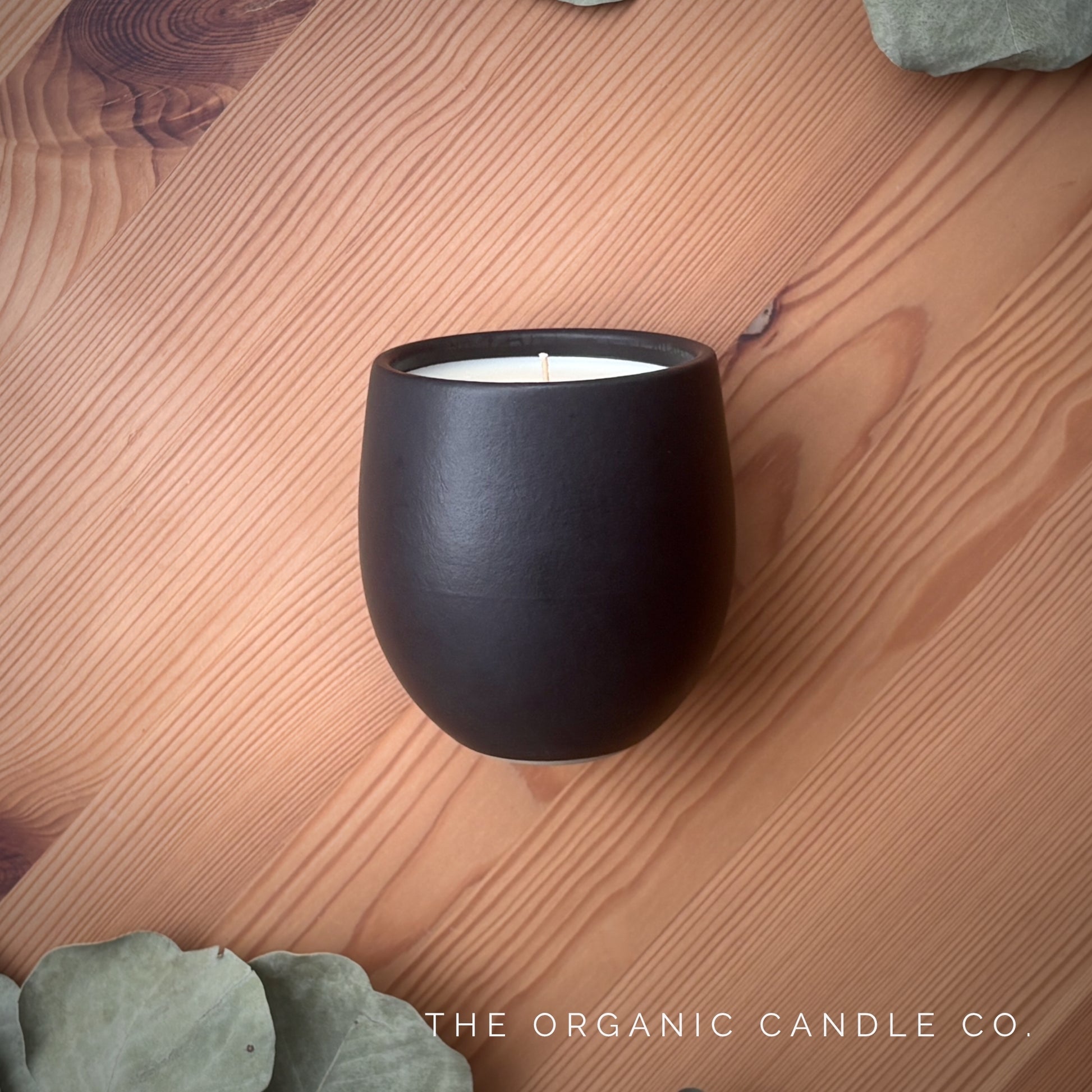Organic candle in black ceramic vessel on a wooden surface with 'The Organic Candle Co' branding.