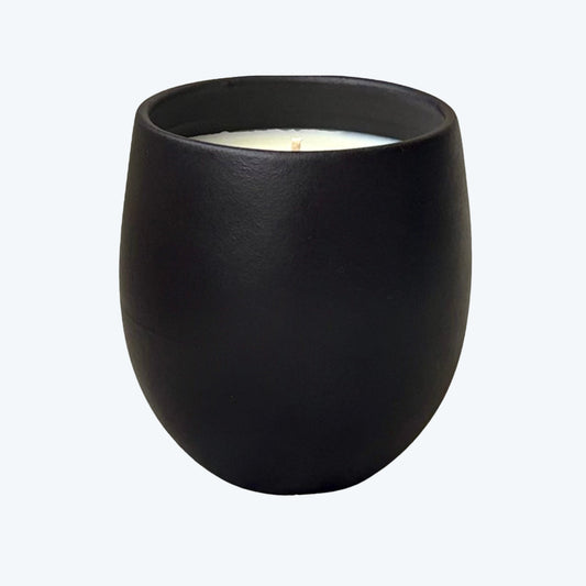 Organic candle in black ceramic vessel on a neutral background