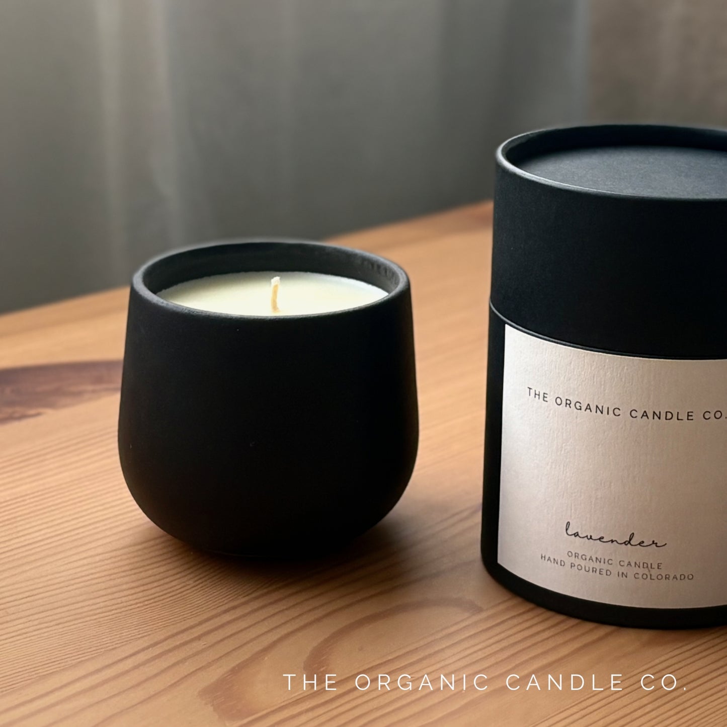 Organic candle in black ceramic vessel and packaging of The Organic Candle Co on a wooden surface