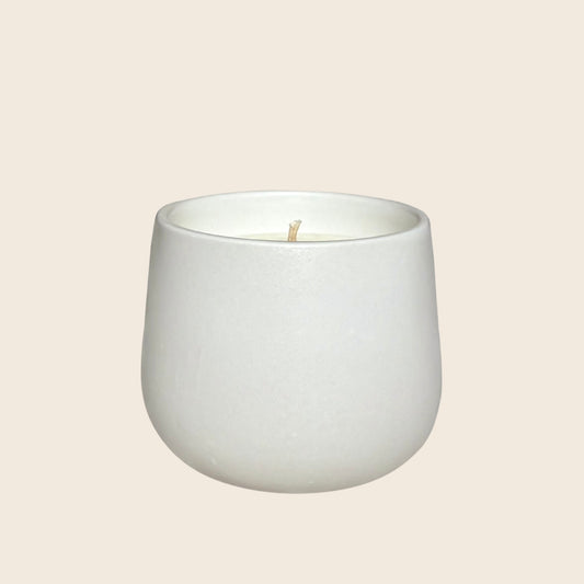 White organic candle in a ceramic vessel on a neutral background