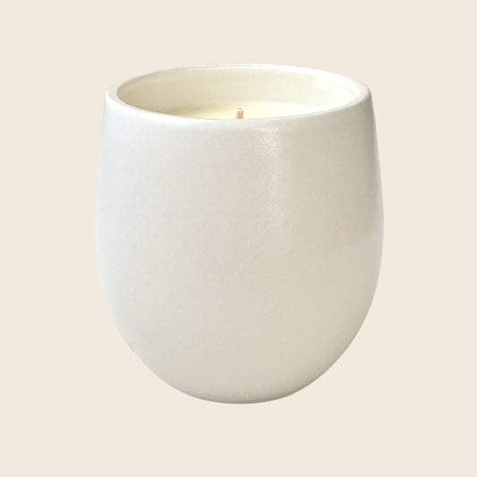 White organic candle in ceramic container on a neutral background