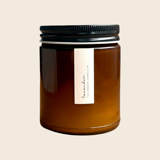 Organic candle in an amber glass vessel with a black lid on a neutral background