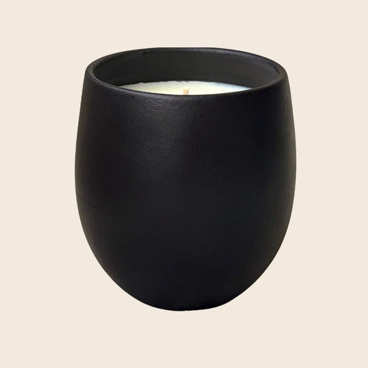 Organic candle in black ceramic vessel on a neutral background