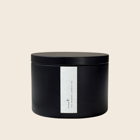 Organic candle in a black metal jar with a white label on a neutral background