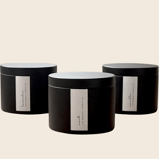 Three organic candles in black cylindrical containers with white labels on a neutral background